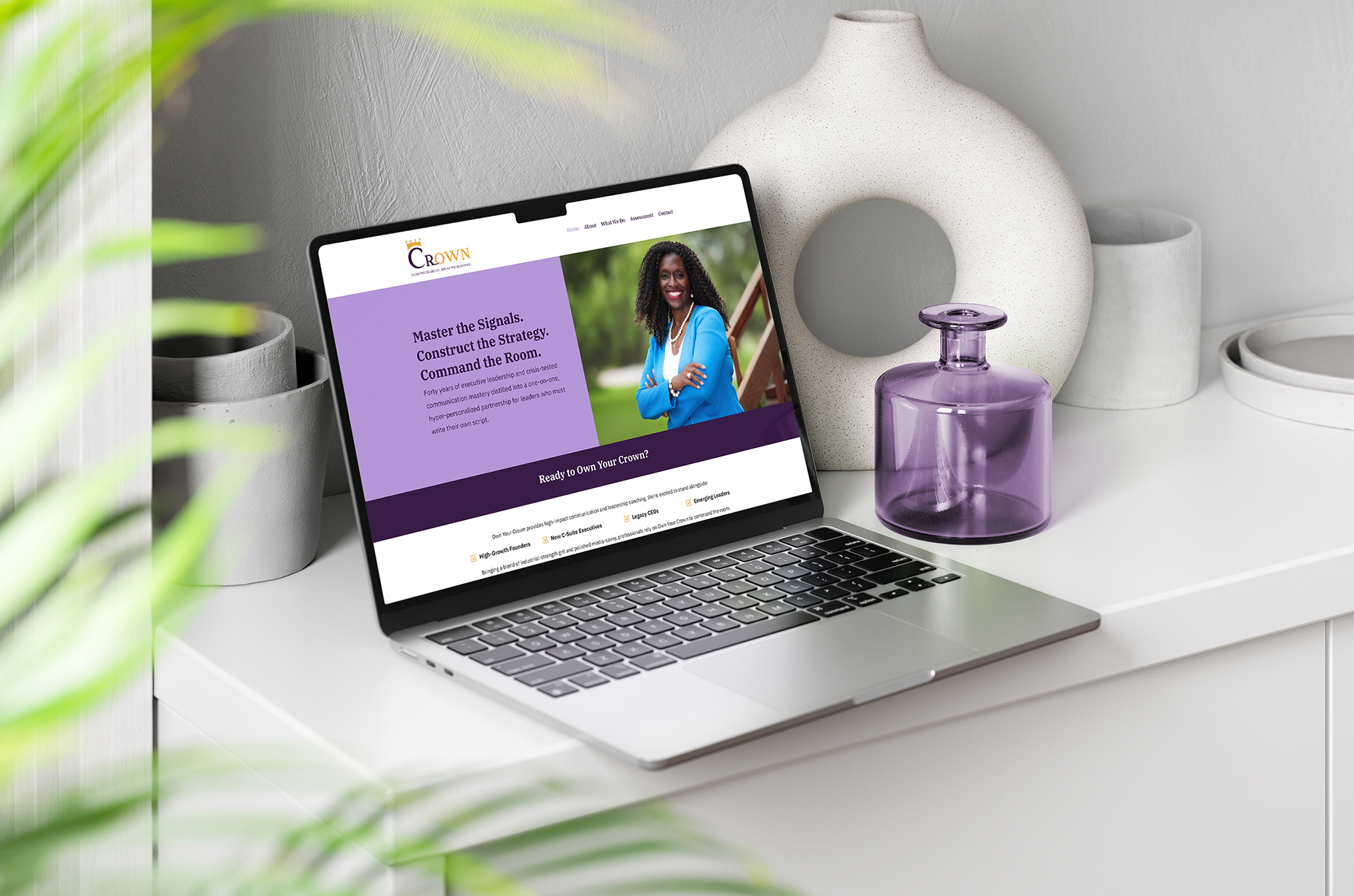 Own Your Crown-Laptop on Dresser with Vase-Mockup-Landscape A screenshot of the Own Your Crown website designed by Gray Creative Studio mocked up on a laptop. The laptop is sitting on a dresser with some vases behind it and some leaves from a tree are blurred out in the foreground of the image.